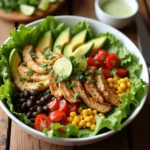 chicken taco salad featuring seasoned grilled chicken slices, avocado, cherry tomatoes, black beans, corn, and fresh lettuce, garnished with cilantro and lime wedges.