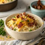 A creamy bowl of crack chicken pasta with shredded cheese, crispy bacon, and fresh parsley on top.