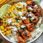 Close-up of a Street Corn Chicken Rice Bowl with grilled charred chicken pieces, fluffy white rice, creamy Mexican street corn, lime wedges, and fresh cilantro topping