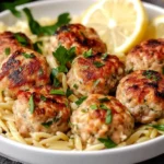 Greek Chicken Meatballs with Lemon Orzo served in a white bowl with lemon slices and parsley garnish.