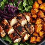 Blackened Chicken and Sweet Potato Bowls with roasted sweet potatoes, greens, and seared chicken breast in a black bowl.