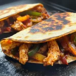 Blackstone Chicken Fajita Quesadillas sizzling on a hot griddle with melted cheese, chicken strips, and colorful peppers.