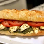 Close-up of a Chicken Pesto Sandwich with grilled chicken, fresh tomato slices, and pesto on a toasted ciabatta roll.