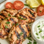 Grilled Greek Yogurt Marinated Chicken served with fresh herbs, cherry tomatoes, lemon wedges, and creamy yogurt sauce.