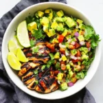 Grilled Chicken with Avocado Salsa served with lime wedges and fresh cilantro in a white bowl.
