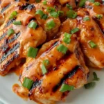 Grilled Honey Buffalo Chicken Thighs with sauce and green onions on a white plate
