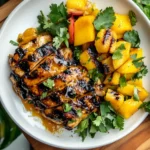 Sliced Grilled Mango Chicken served with grilled mango chunks and fresh cilantro on a white plate