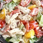 Close-up of creamy Italian Grinder Chicken Salad with grape tomatoes, shredded chicken, banana peppers, and romaine lettuce in a black bowl.