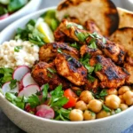 Colorful Spicy Chicken Nourish Bowl topped with grilled chicken, chickpeas, couscous, fresh veggies, and flatbread.