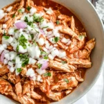 Bowl of shredded Chicken Tinga topped with chopped onions and fresh cilantro.