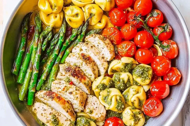 Colorful skillet of Pesto Chicken with Tortellini and Veggies featuring asparagus, cherry tomatoes, and sliced chicken.