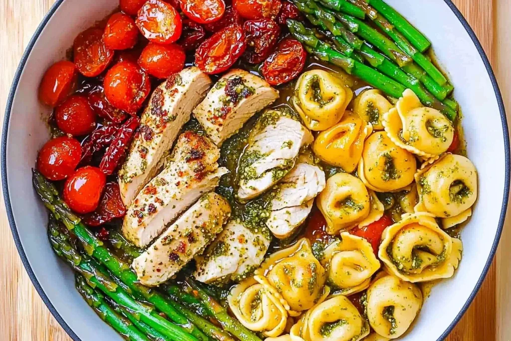Pesto Chicken with Tortellini and Veggies served with asparagus and cherry tomatoes in a white skillet.