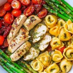 Pesto Chicken with Tortellini and Veggies served with asparagus and cherry tomatoes in a white skillet.