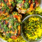 Close-up of grilled Chimichurri Chicken Thighs served in a bowl with extra chimichurri sauce on the side.