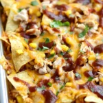 Close-up of Sheet Pan BBQ Chicken Nachos loaded with cheese, shredded chicken, corn, and BBQ sauce.