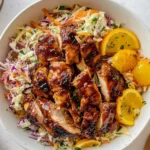Hot honey BBQ chicken thighs served over fresh citrus slaw in a white bowl – a colorful BBQ chicken with citrus slaw dish.
