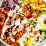 Colorful BBQ Chicken Salad topped with ranch dressing, avocado, corn, and fresh vegetables in a white bowl.