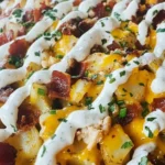 Close-up of Blackstone Buffalo Chicken Loaded Potatoes topped with bacon, cheddar cheese, ranch drizzle, and fresh herbs.