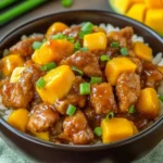 Bowl of Chinese-Style Mango Chicken Stir Fry served over rice with fresh mango chunks and green onions.