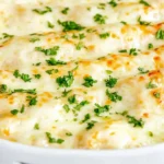 Baked White Chicken Enchilada Casserole covered in melted cheese and garnished with fresh parsley in a white dish.