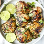Grilled cilantro lime chicken thighs garnished with fresh cilantro and lime slices on a white plate.
