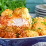 A close-up of Cheddar Bay Chicken Bake showing a juicy piece of chicken topped with cheesy biscuit crust and marinara sauce.