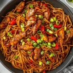 Close-up of Hoisin Chicken with Noodles in a skillet, topped with green onions and red bell peppers.