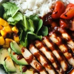 High Protein BBQ Chicken Ranch Bowl with sliced grilled chicken, avocado, mango, greens, tomatoes, and rice drizzled in BBQ sauce.