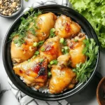 Vietnamese Lemongrass Chicken served over rice, topped with herbs and scallions in a black bowl.