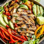 Grilled Healthy Chili Lime Chicken Fajita bowl with avocado, bell peppers, and lime wedges on a bed of fresh lettuce.