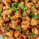 Close-up of Ground Orange Chicken with spicy glaze and chopped green onions over rice