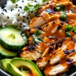 Close-up of Spicy Honey-Ginger Chicken Bowls with Yum Yum Sauce, served with rice, avocado, and cucumber slices.