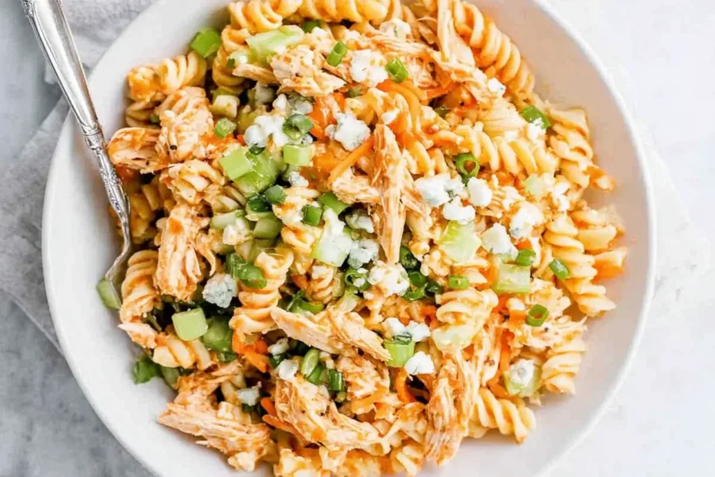 Close-up of Buffalo Chicken Pasta Salad with shredded chicken, rotini, celery, green onions, and crumbled blue cheese.