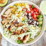 Baja Chicken Bowls with grilled chicken, corn, black beans, avocado, and cilantro sauce on a rustic wooden table