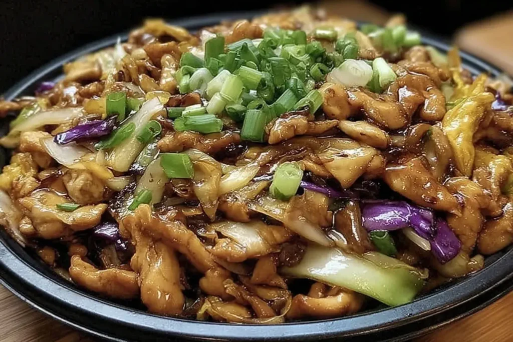 Moo Shu Chicken Recipe with tender chicken, colorful cabbage, and savory sauce, garnished with fresh green onions in a black serving dish.