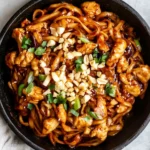 Kung Pao Chicken Noodles topped with crushed peanuts and green onions in a black bowl