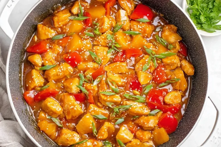 “Hawaiian Chicken with pineapple chunks and red peppers in a savory sauce, garnished with sesame seeds and green onions in a skillet.