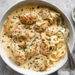 Tender Crockpot Angel Chicken with creamy sauce and angel hair pasta in a white bowl, garnished with parsley and red pepper flakes.