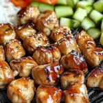 Glazed chicken bites on a Blackstone griddle with rice and cucumbers from a Blackstone Griddle Hibachi Chicken Feast.