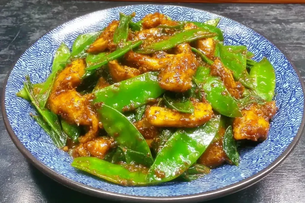 Chicken and Snow Peas Stir Fry with tender chicken slices and crisp snow peas coated in savory sauce on a blue plate