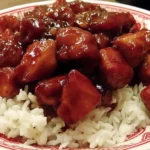 Food Court Bourbon Chicken served over white rice on a decorative red and white plate.