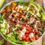 Fresh and colorful Loaded Burger Bowl with ground beef, bacon, avocado, tomatoes, and special sauce drizzle.