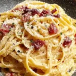 Stanley Tucci’s Pasta Carbonara served on a black plate, featuring creamy spaghetti, crispy pancetta, and grated Pecorino Romano.
