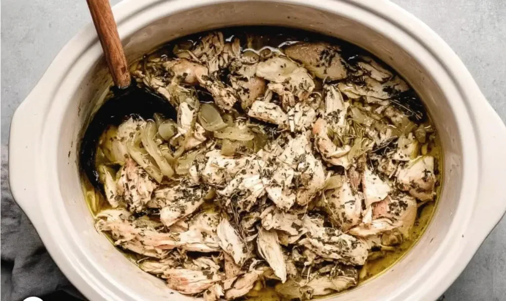 Slow Cooker Greek Chicken shredded in a crockpot with onions, herbs, and flavorful lemon garlic broth.
