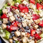 Strawberry Poppyseed Chicken Salad featuring chunks of chicken, strawberries, blueberries, pecans, feta, and creamy poppyseed dressing on romaine lettuce.