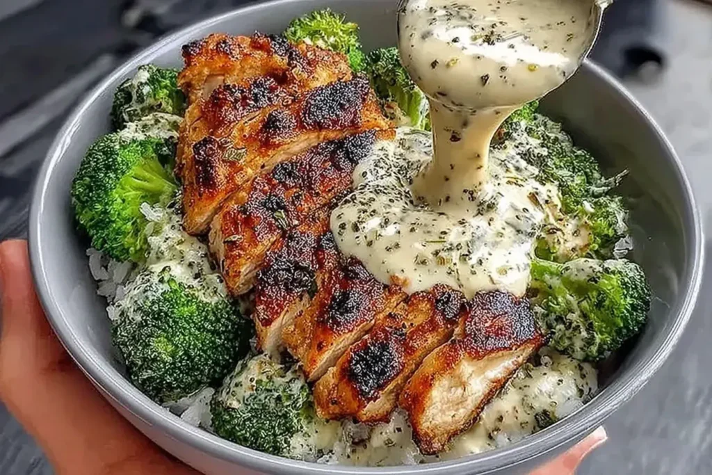Grilled Chicken Broccoli Bowls with Creamy Garlic Sauce featuring sliced grilled chicken, steamed broccoli, rice, and herb-speckled garlic sauce being poured.