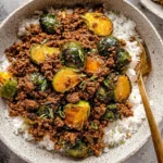 Ground Beef and Brussels Sprouts served over white rice in a bowl, topped with green onions and a savory sauce.