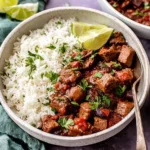 Carne Picada served with white rice, lime wedges, and fresh cilantro in a ceramic bowl
