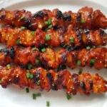 Charred Korean Chicken Skewers garnished with sesame seeds and green onions on a white platter.