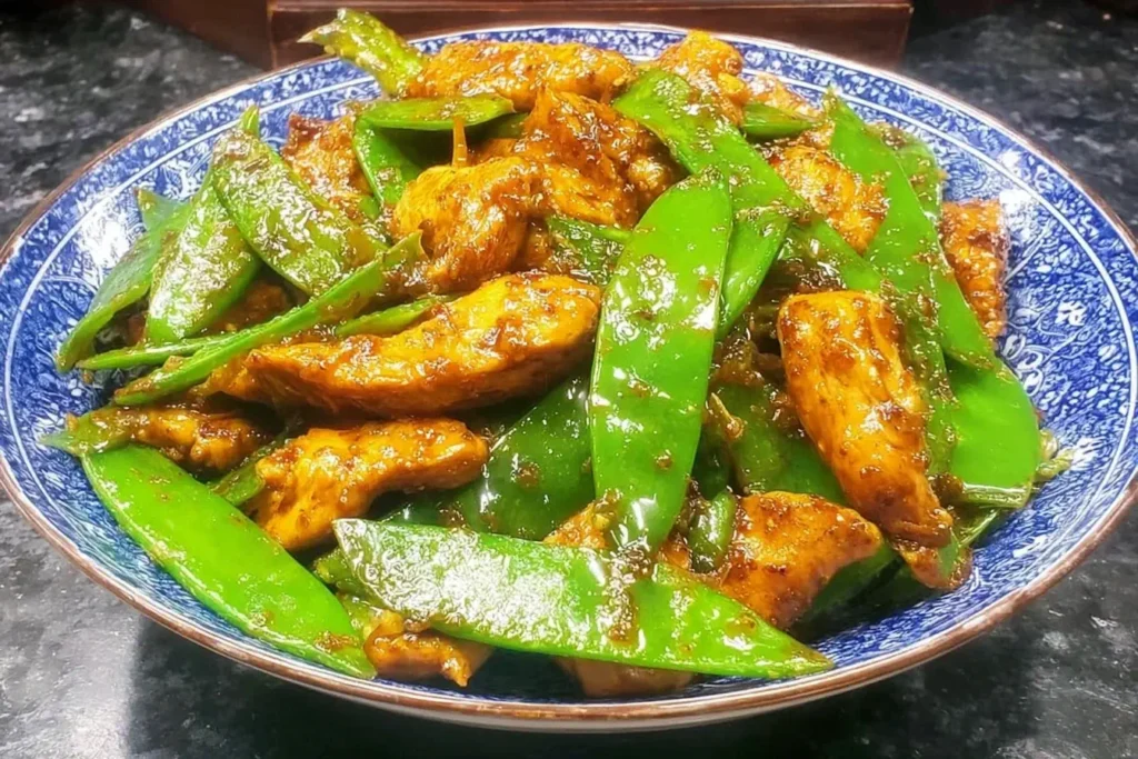 Chicken and Snow Peas Stir Fry featuring juicy chicken strips and crisp snow peas coated in savory sauce on a patterned blue bowl.